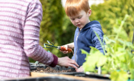 A young boy works in his ECE classroom’s outdoor gardening space, along with his caregiver.