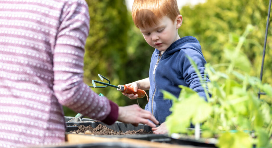 A young boy works in his ECE classroom’s outdoor gardening space, along with his caregiver.