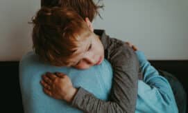 A young boy, with a worried expression, receives a comforting hug from his caregiver.