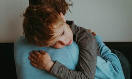 A young boy, with a worried expression, receives a comforting hug from his caregiver.
