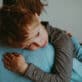 A young boy, with a worried expression, receives a comforting hug from his caregiver.