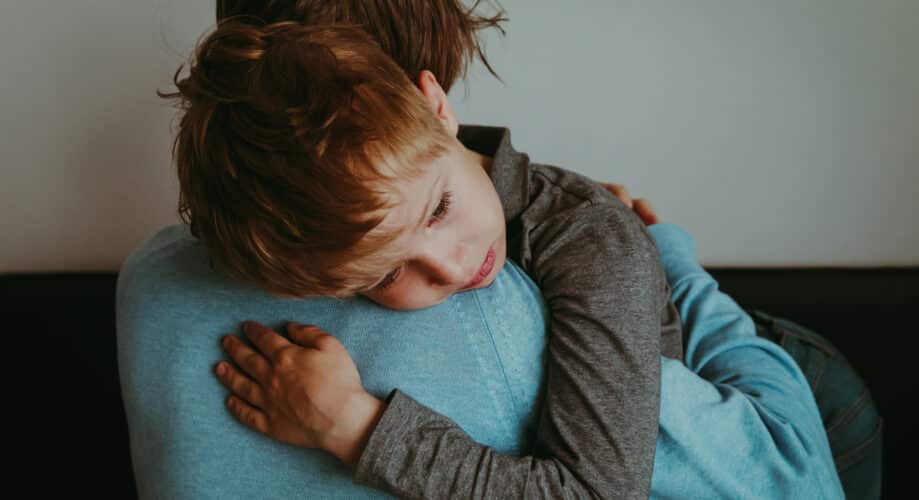 A young boy, with a worried expression, receives a comforting hug from his caregiver.