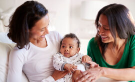 A baby boy sits on his mother’s lap, alongside another caregiver.