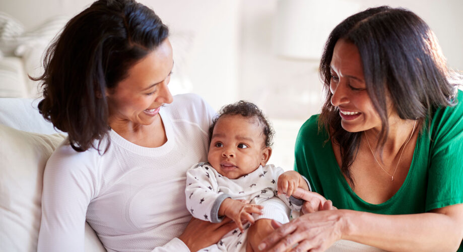 A baby boy sits on his mother’s lap, alongside another caregiver.