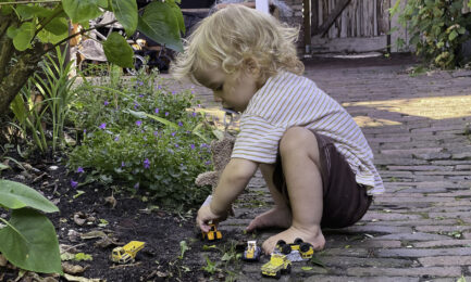 A toddler boy plays with toy cars and trucks outdoors.
