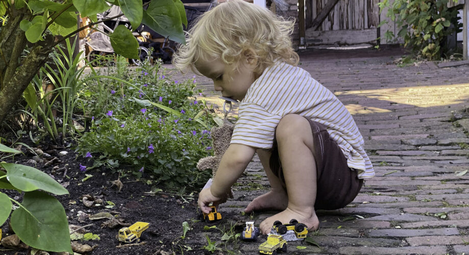 A toddler boy plays with toy cars and trucks outdoors.