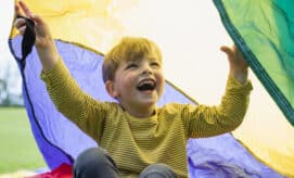 A young boy plays outdoors with a parachute.