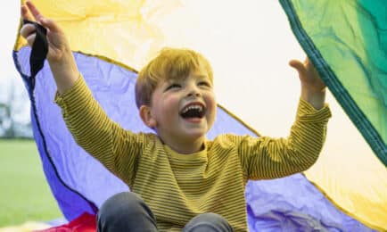 A young boy plays outdoors with a parachute.