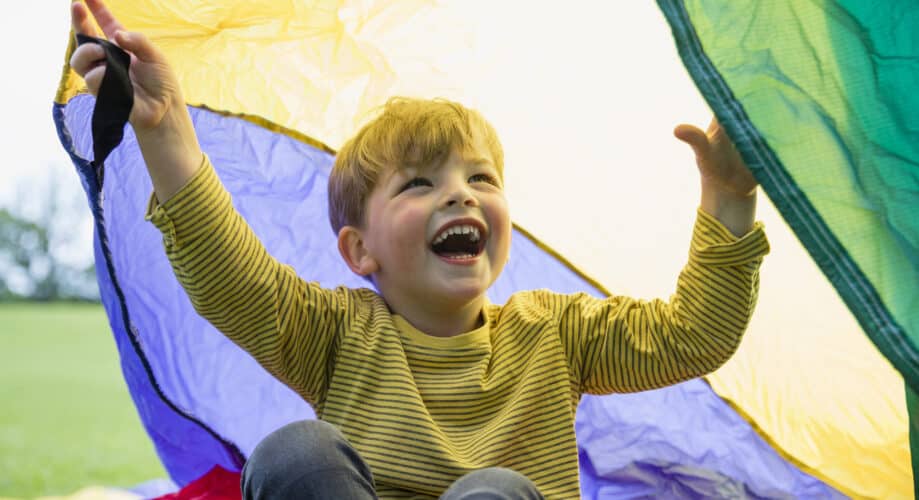 A young boy plays outdoors with a parachute.