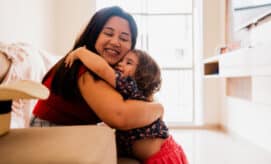 A toddler girl hugs her caregiver.