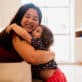 A toddler girl hugs her caregiver.