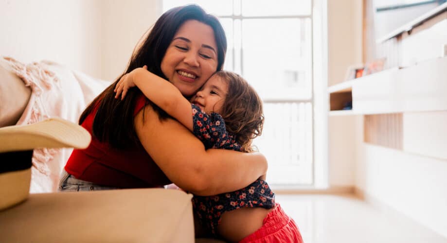 A toddler girl hugs her caregiver.