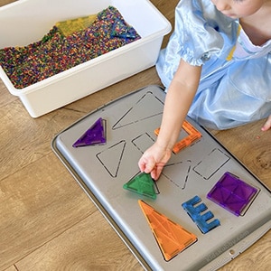 young child placing shapes onto drawn outlines of matching shapes on the back of a baking sheet