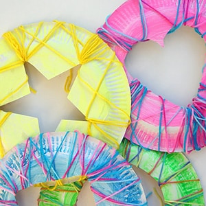 paper plates decorated by young children using marker colors, yarn, and cutout shapes like hearts, stars, circles and squares