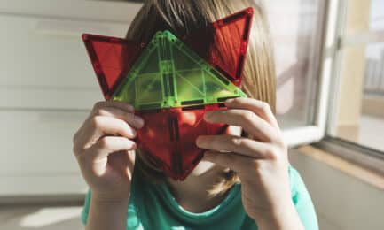 A child smiles while holding magnatiles.