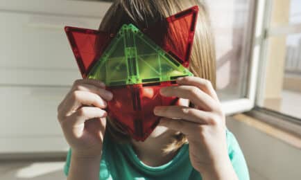 A child smiles while holding magnatiles.