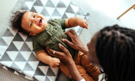 A baby lies on his back and laughs with his caregiver.