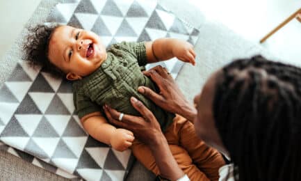 A baby lies on his back and laughs with his caregiver.