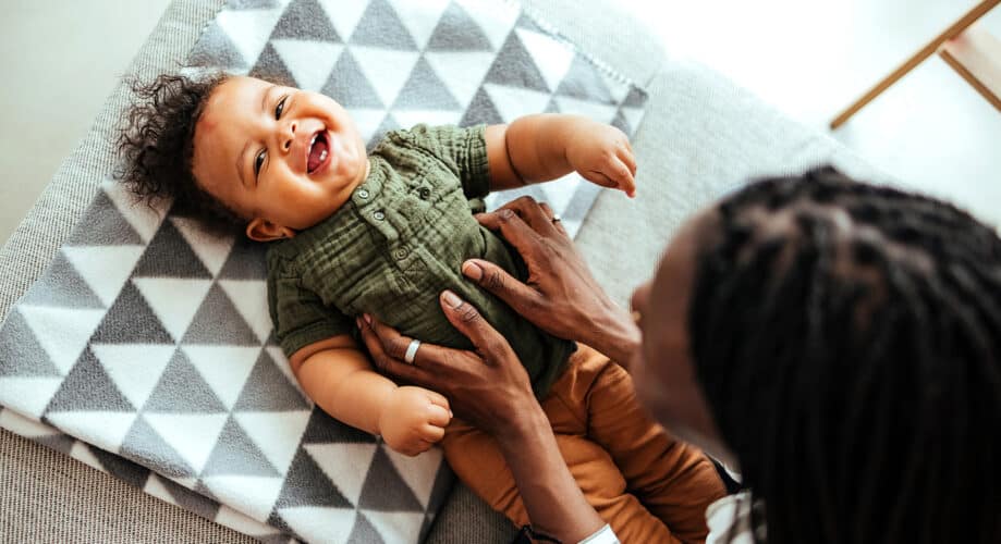 A baby lies on his back and laughs with his caregiver.
