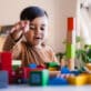 A toddler boy plays with blocks and wooden toys.