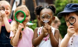 A group of preschool children look through magnifying glasses.