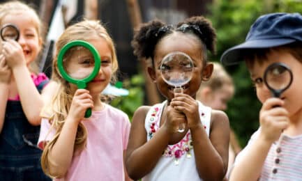 A group of preschool children look through magnifying glasses.
