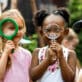 A group of preschool children look through magnifying glasses.