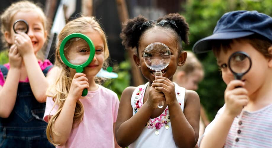 A group of preschool children look through magnifying glasses.