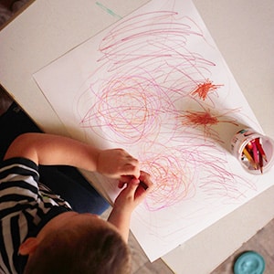 Child draws on paper with crayons.