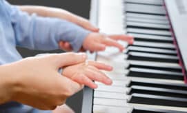 A baby plays piano with their caregiver.