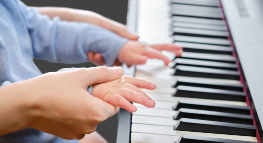 A baby plays piano with their caregiver.