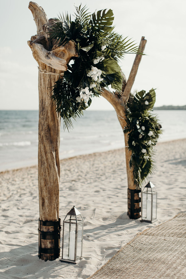 A dramatic driftwood beach wedding arch with palm fronds A dramatic driftwood beach wedding arch with palm fronds