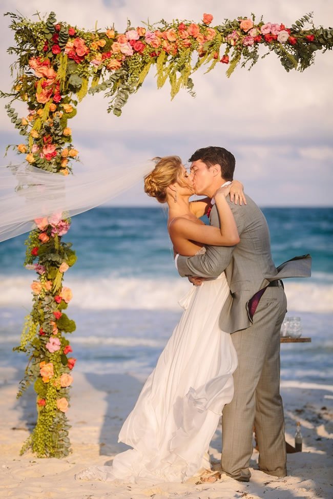 Beach ceremony arch covered in bright flowers and greenery Beach ceremony arch covered in bright flowers and greenery