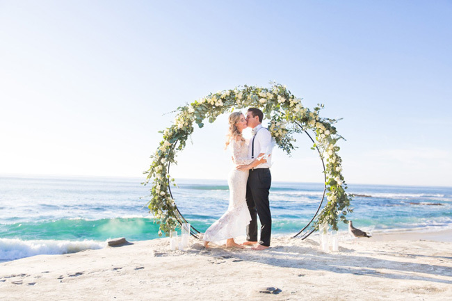 A circular beach wedding arch covered in greenery A circular beach wedding arch covered in greenery