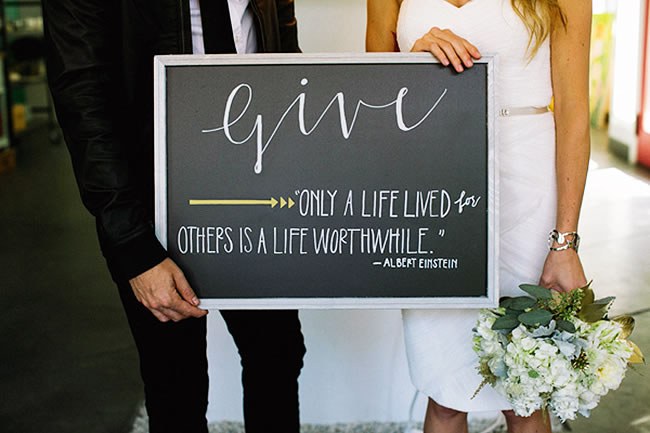 Bride and groom hold a chalkboard sign with an Albert Einstein quote about giving