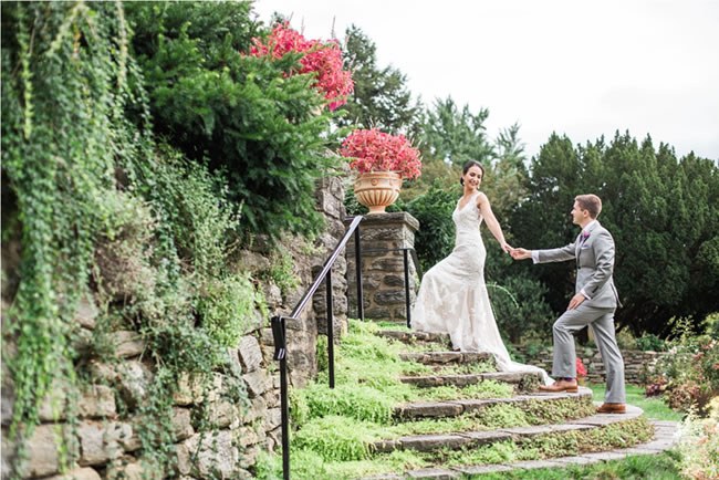 How to have a charitable wedding Bride and groom walk up moss-covered stairs at Morris Arboretum in Pennsylvania