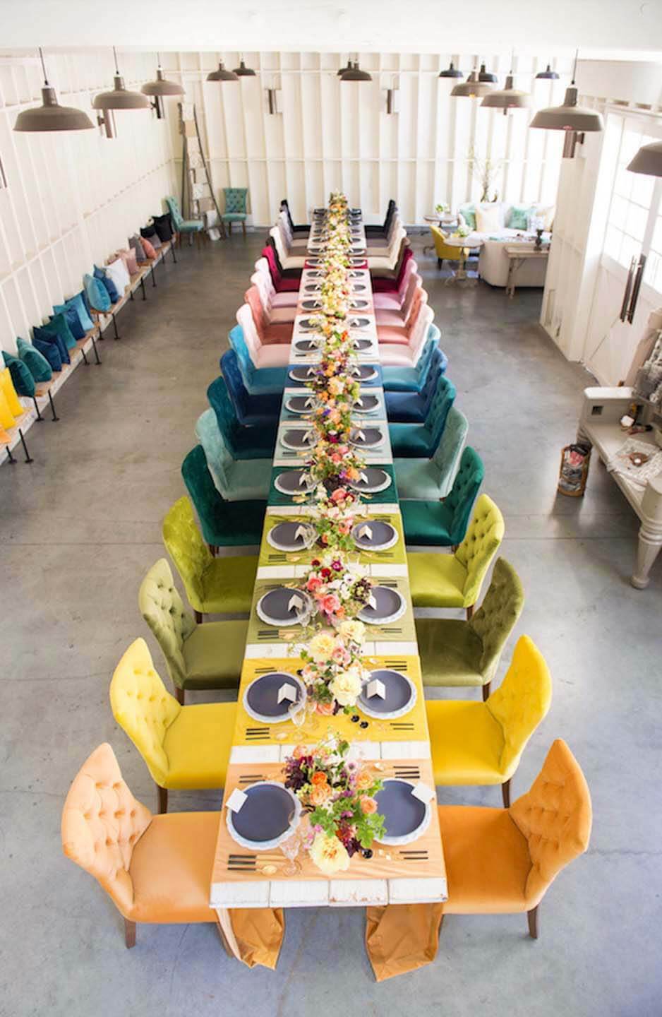 An ombre assortment of colorful velvet chairs and table settings with matching throw pillows