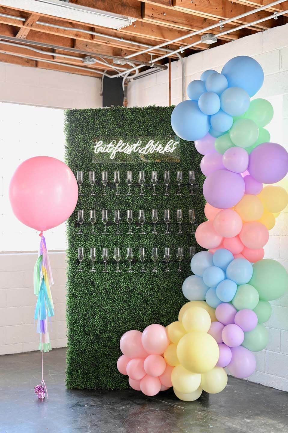 A pastel rainbow balloon installation accents a greenery champagne wall