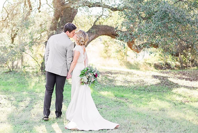 Newlyweds kiss in a beautiful shady grove in Dripping Springs Texas