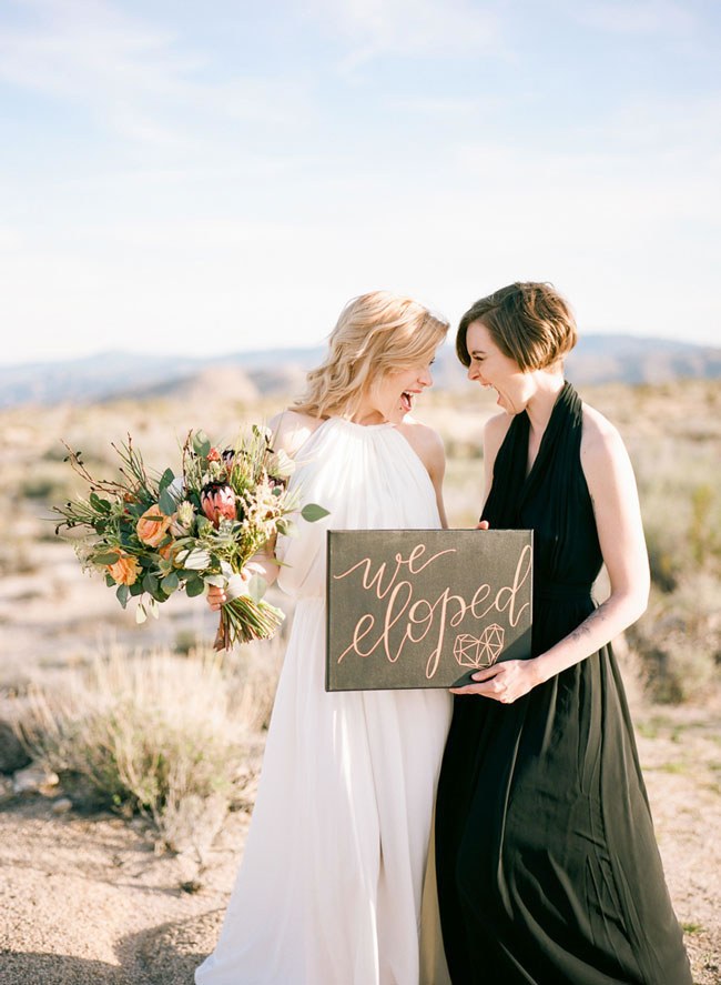 Two joyful brides hold a 'We Eloped' sign