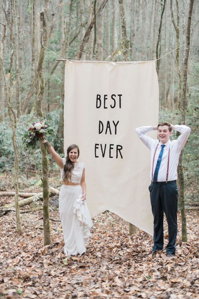 Couple at a forest wedding pose in front of a huge 'Best Day Ever' banner