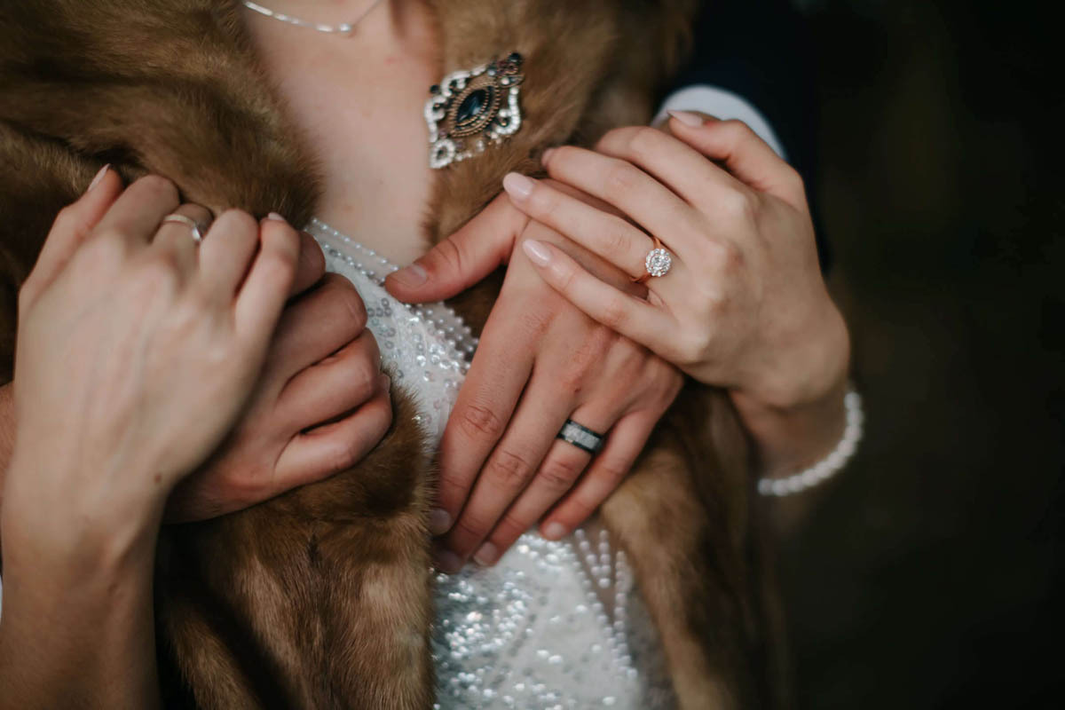 Closeup of a bride's fur stole, vintage brooch, and rings