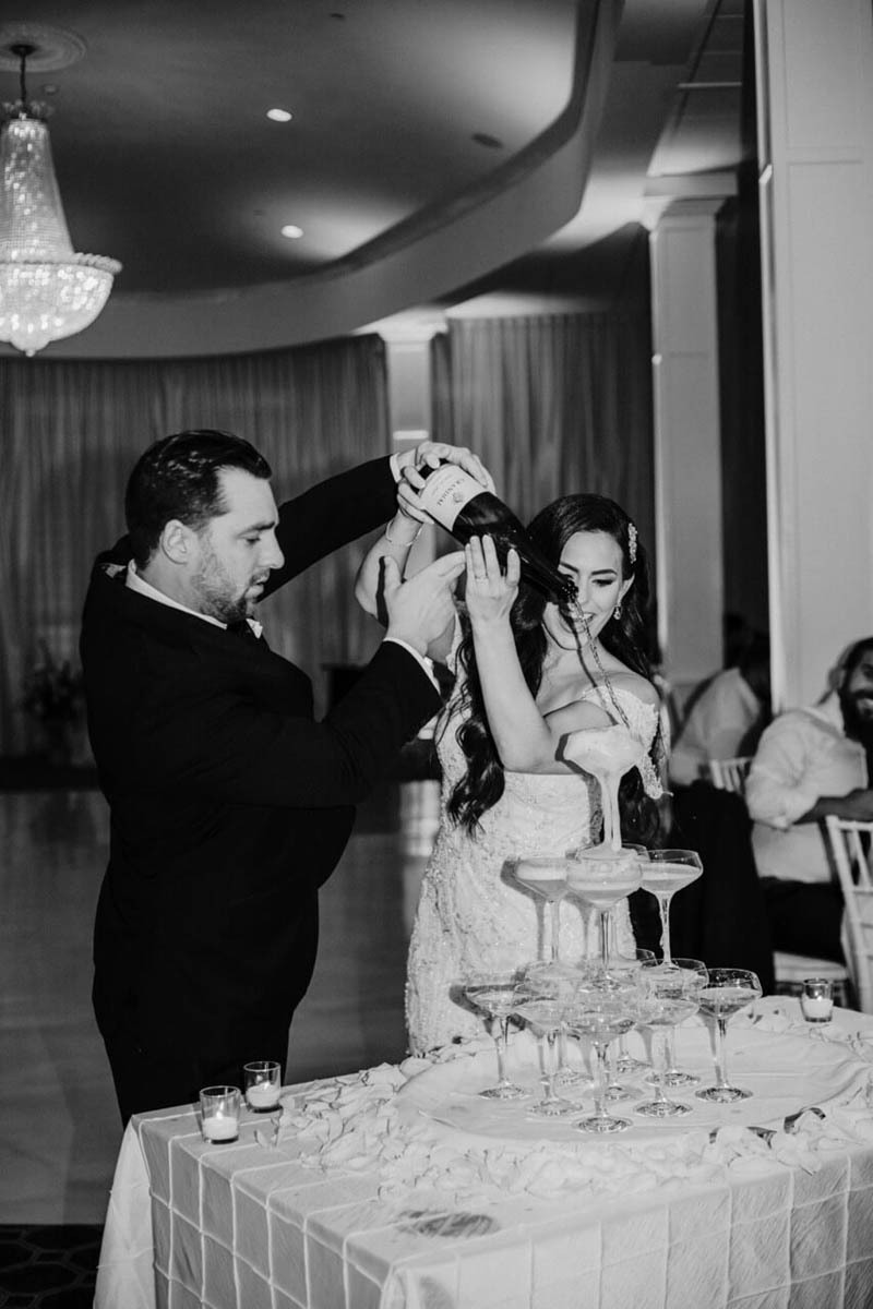 Newlyweds pour a bottle of champagne down a glass tower