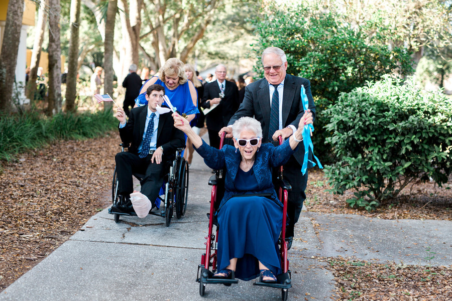 How To Have An Inclusive and Accessible Wedding | A grandma in sunglasses rides her wheelchair to the wedding ceremony excitedly waving ribbon wands