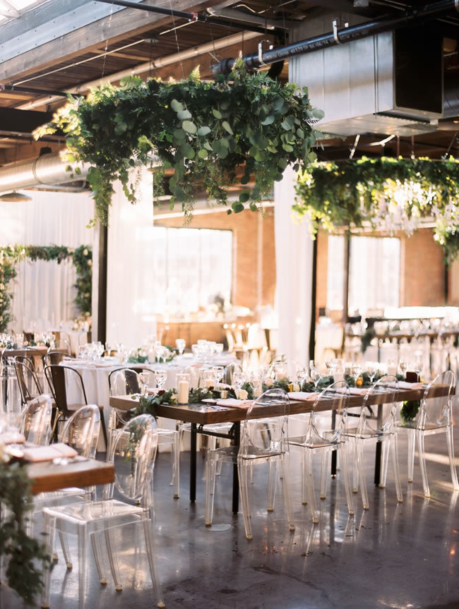 Industrial-chic wedding reception with greenery and ghost chairs