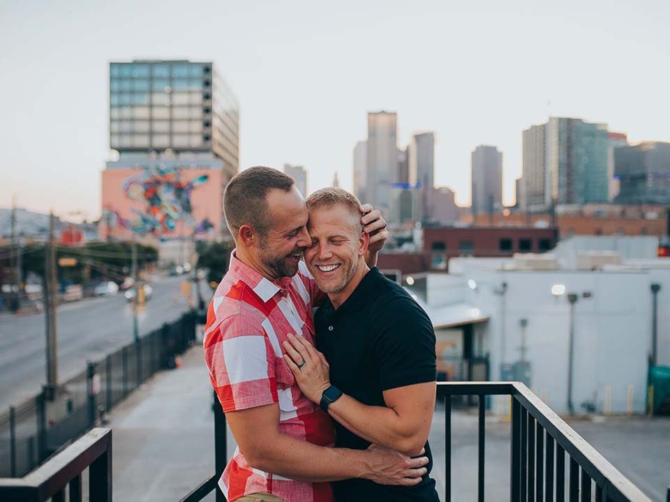 Creative ideas for proposing to your partner | A newly-engaged gay couple embraces on a city rooftop