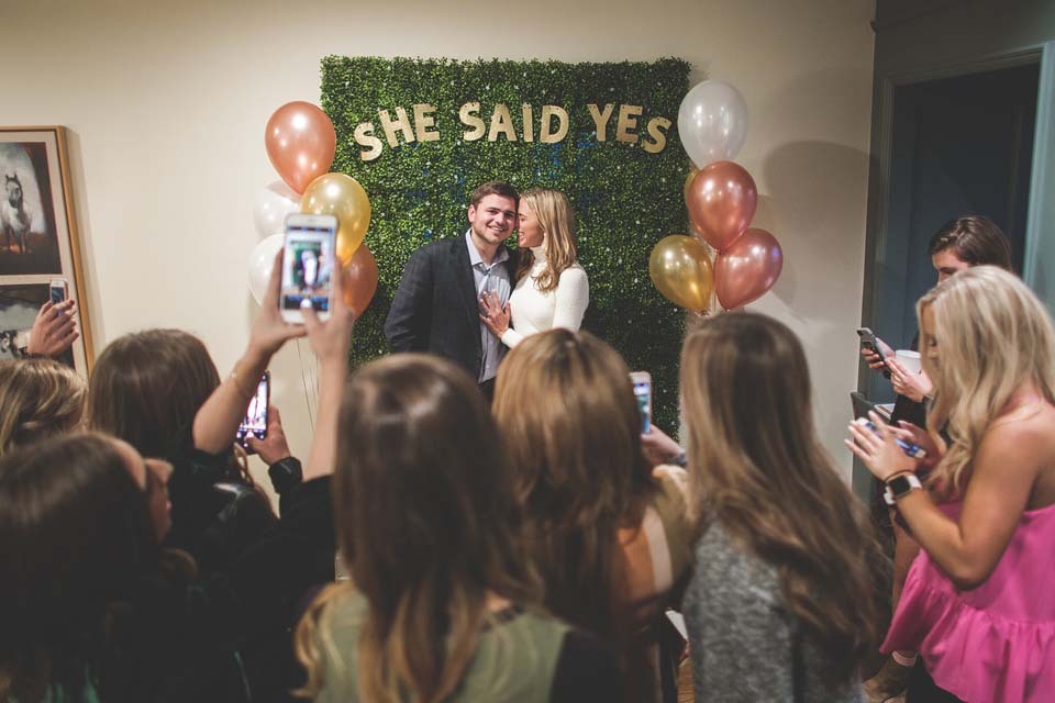Post proposal engagement party with couple posing in front of She Said Yes banner
