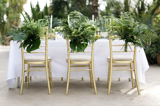 Beach wedding décor idea: Tropical leaves Gold Chiavari chairs with tropical leaves tied to the back