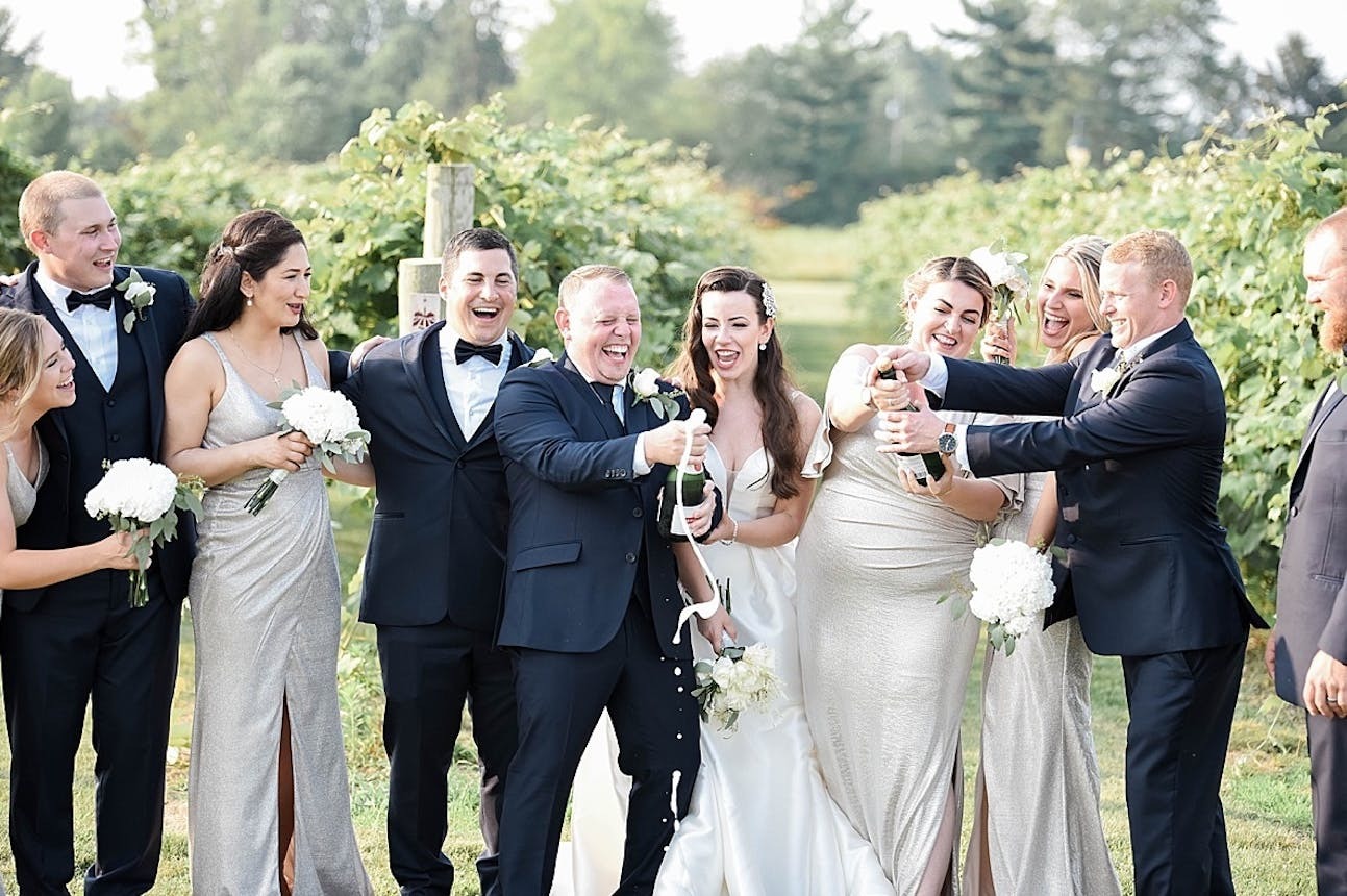 A wedding party pops champagne at The Vineyards at Pine Lake | Wedding Alcohol Costs