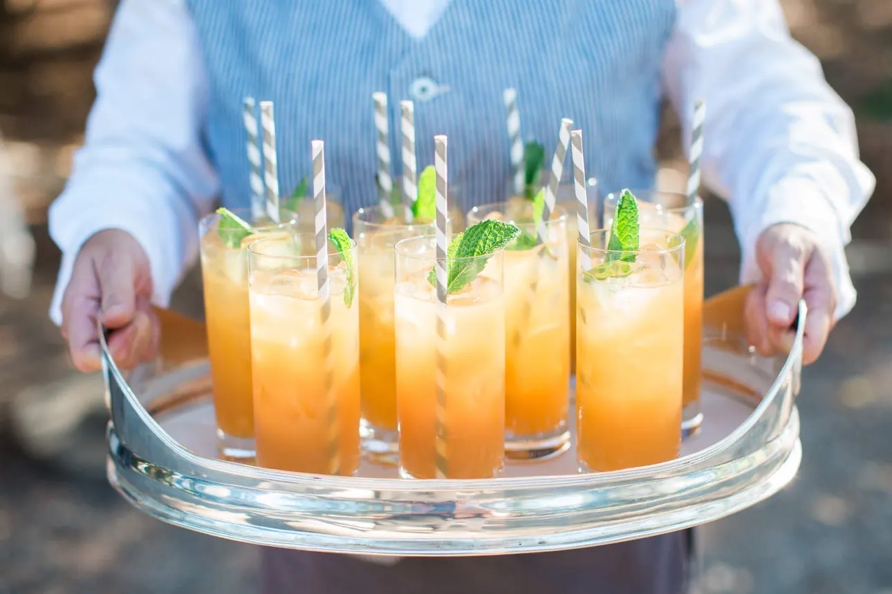 A server carries a tray of summery signature cocktails with striped straws | Everything you need to know about your wedding bar